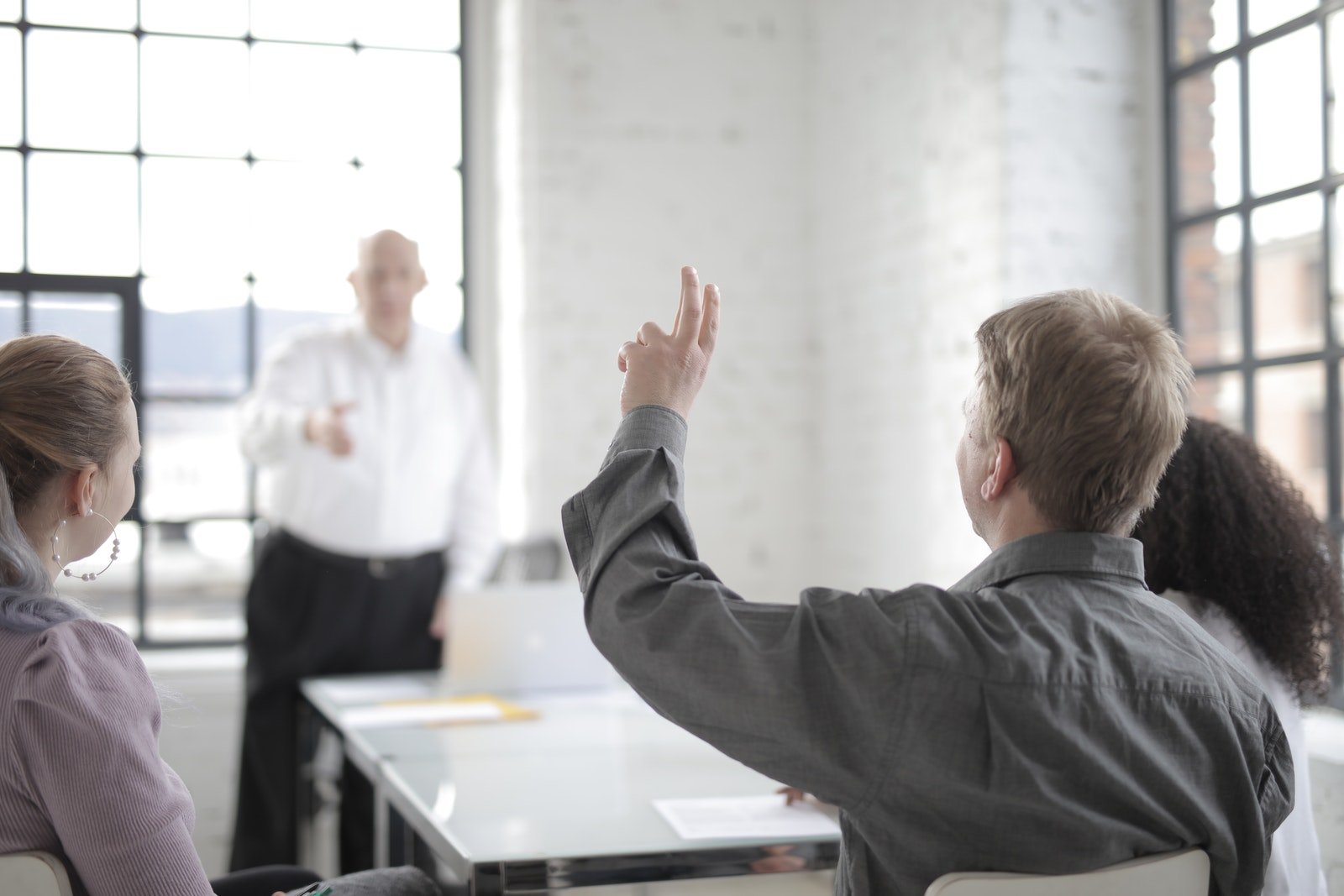 Male employee raising hand for asking question at conference in office boardroom