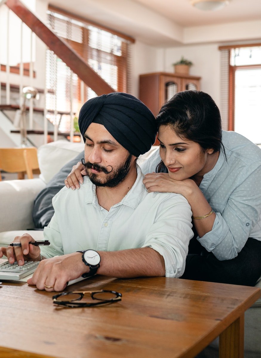 Focused young Indian couple working at home using calculator