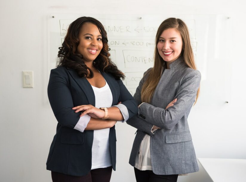 two women in suits standing beside wall