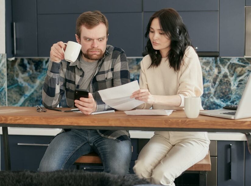 A Man Looking at the Paper while Holding a Coffee and Phone